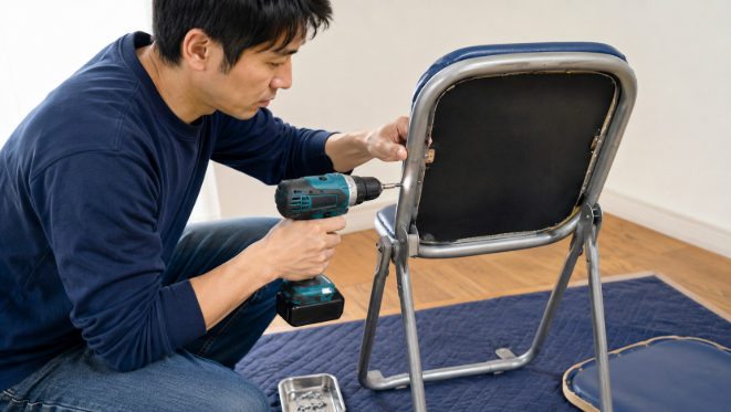 パイプ椅子の生地を張り替えるために電動ドリルを使ってフレームのリベットを取り外すDIY作業